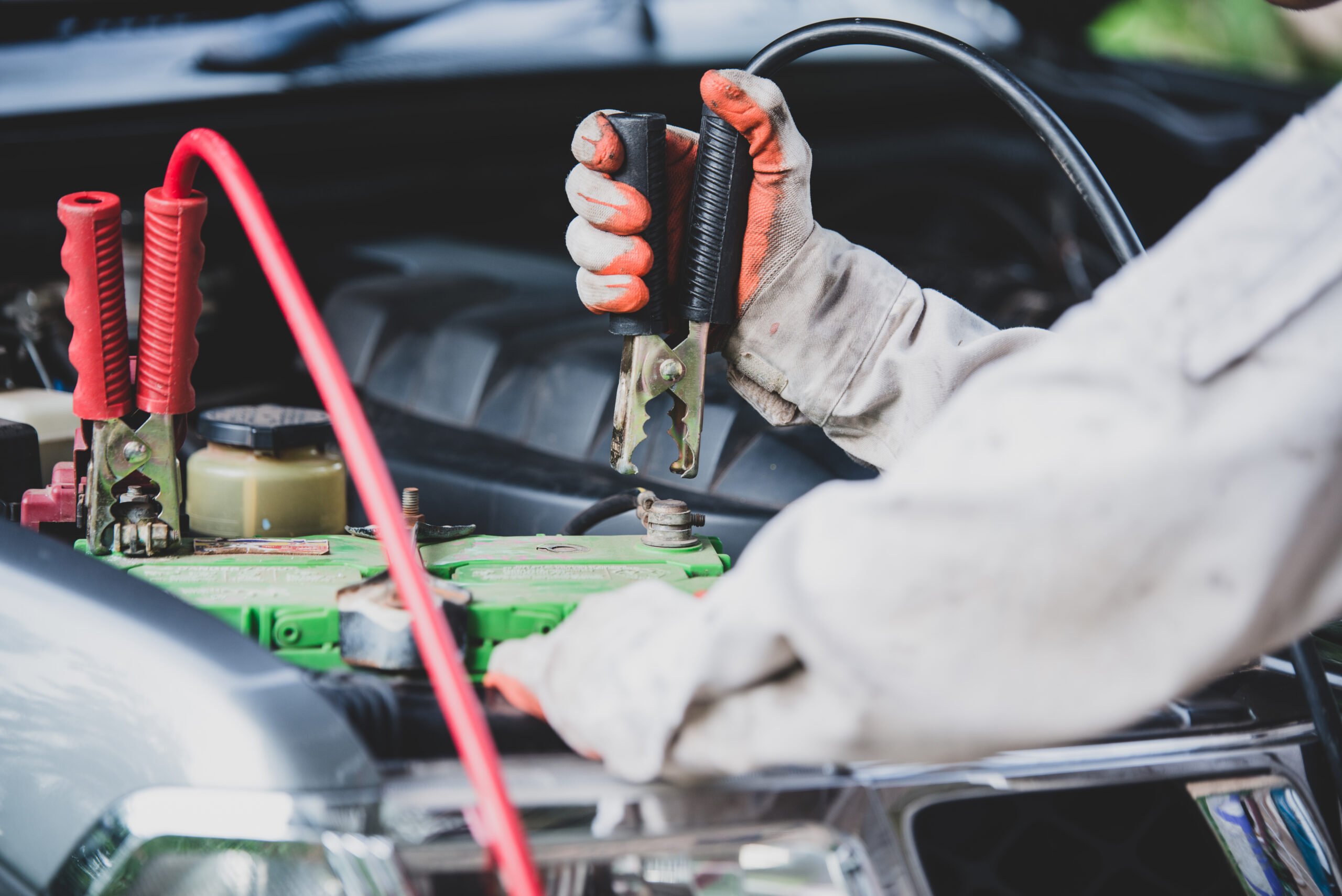 A person jump-starting a car battery with jumper cables.