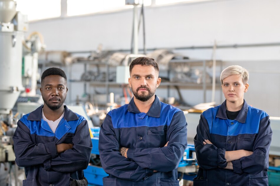 Three factory workers standing with arms crossed in a workshop.