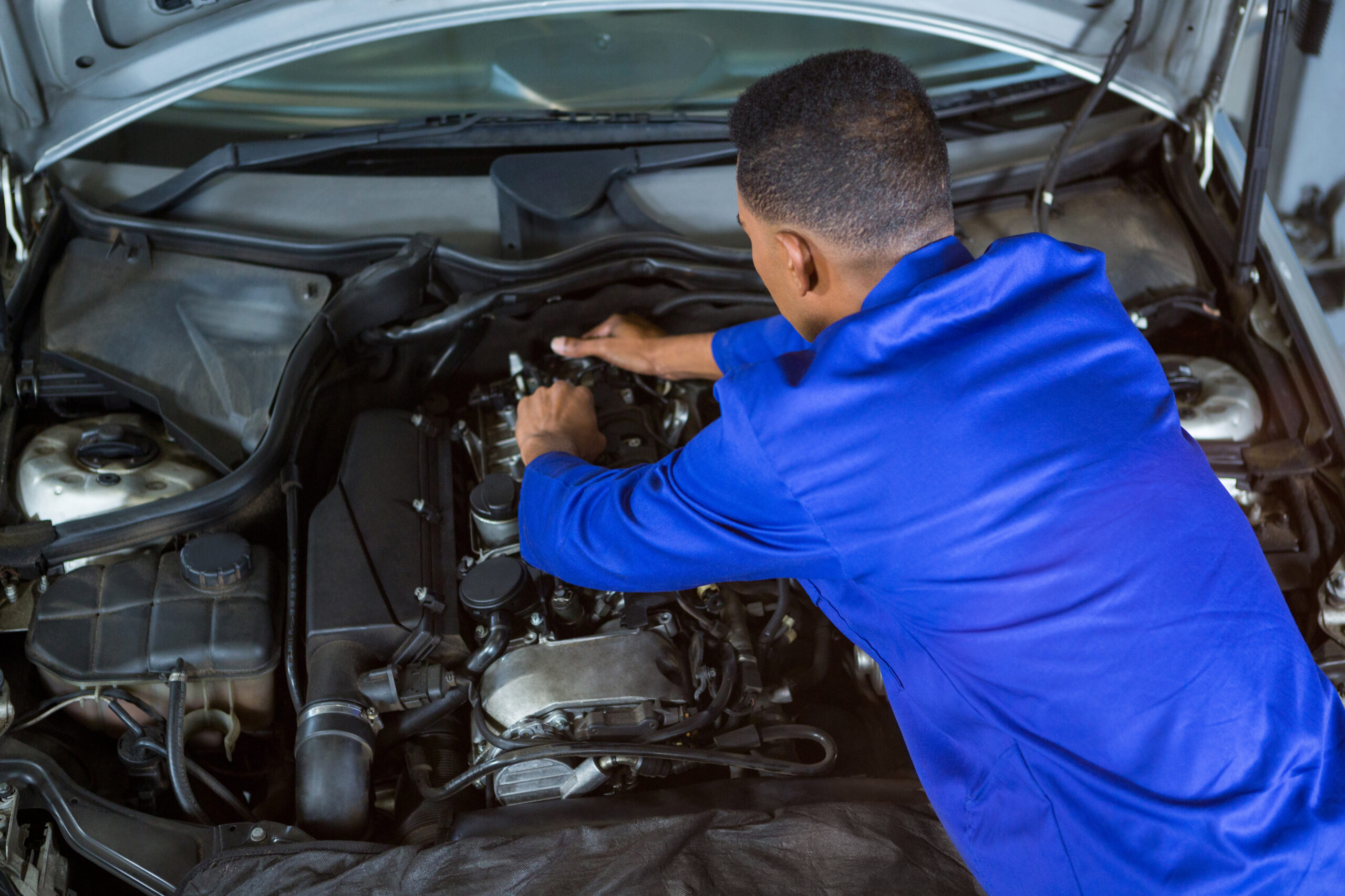 A mechanic in a blue uniform fixing a car engine.